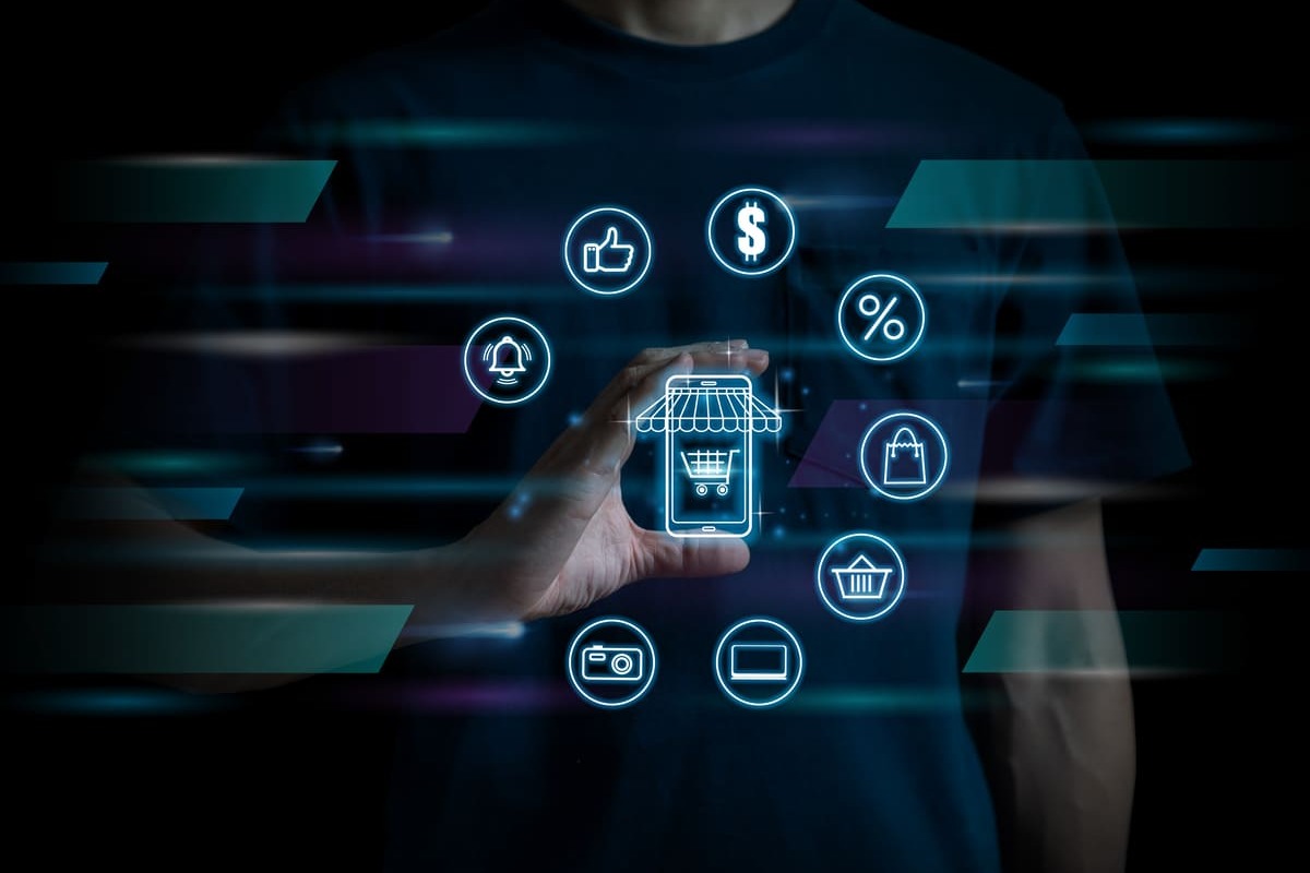 Gemini said Mão segura ícones digitais flutuantes de compras e pagamentos ao redor de um smartphone, representando a transformação digital no varejo.